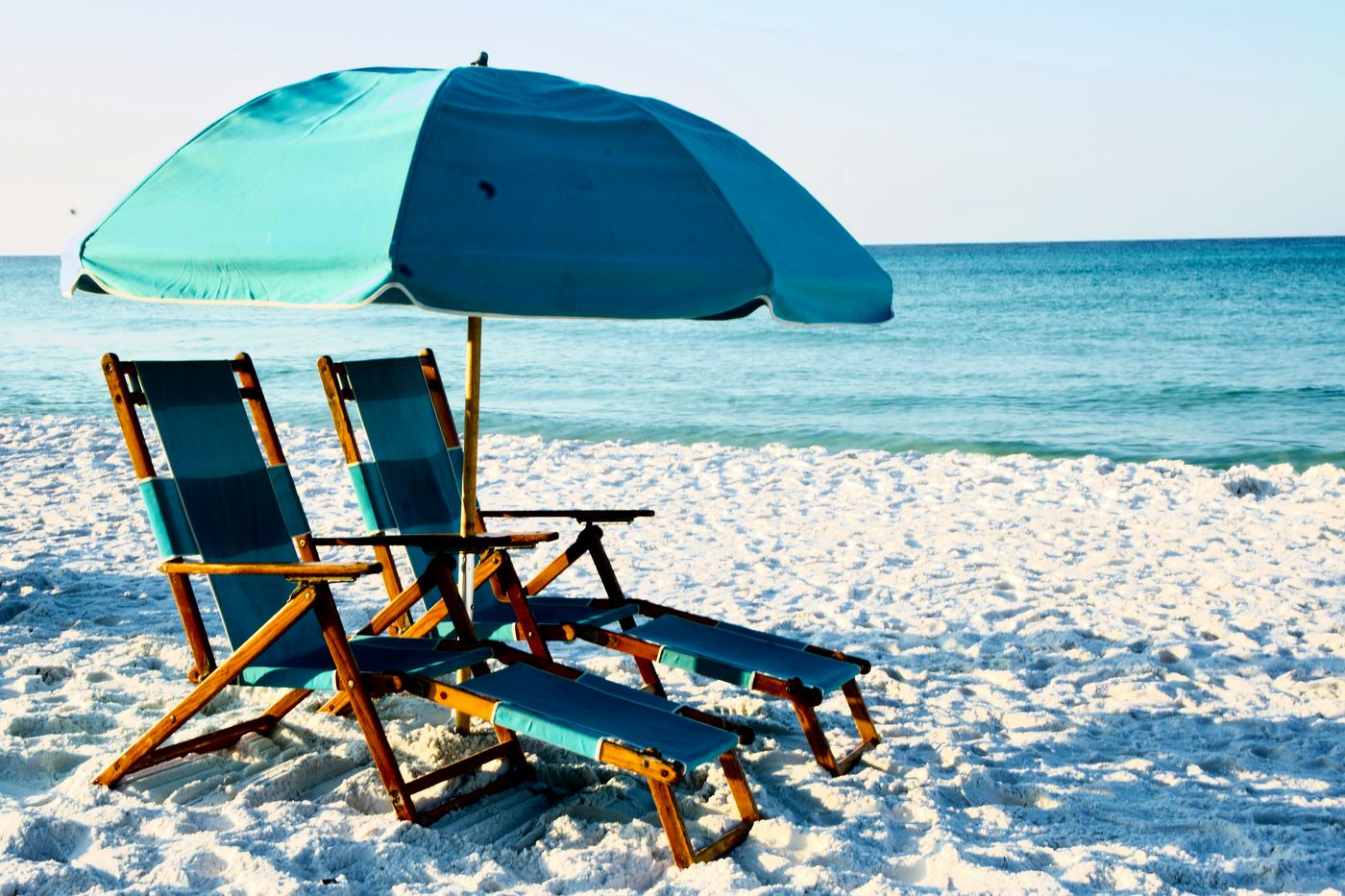 Two wooden beach chairs on white sand facing the water
