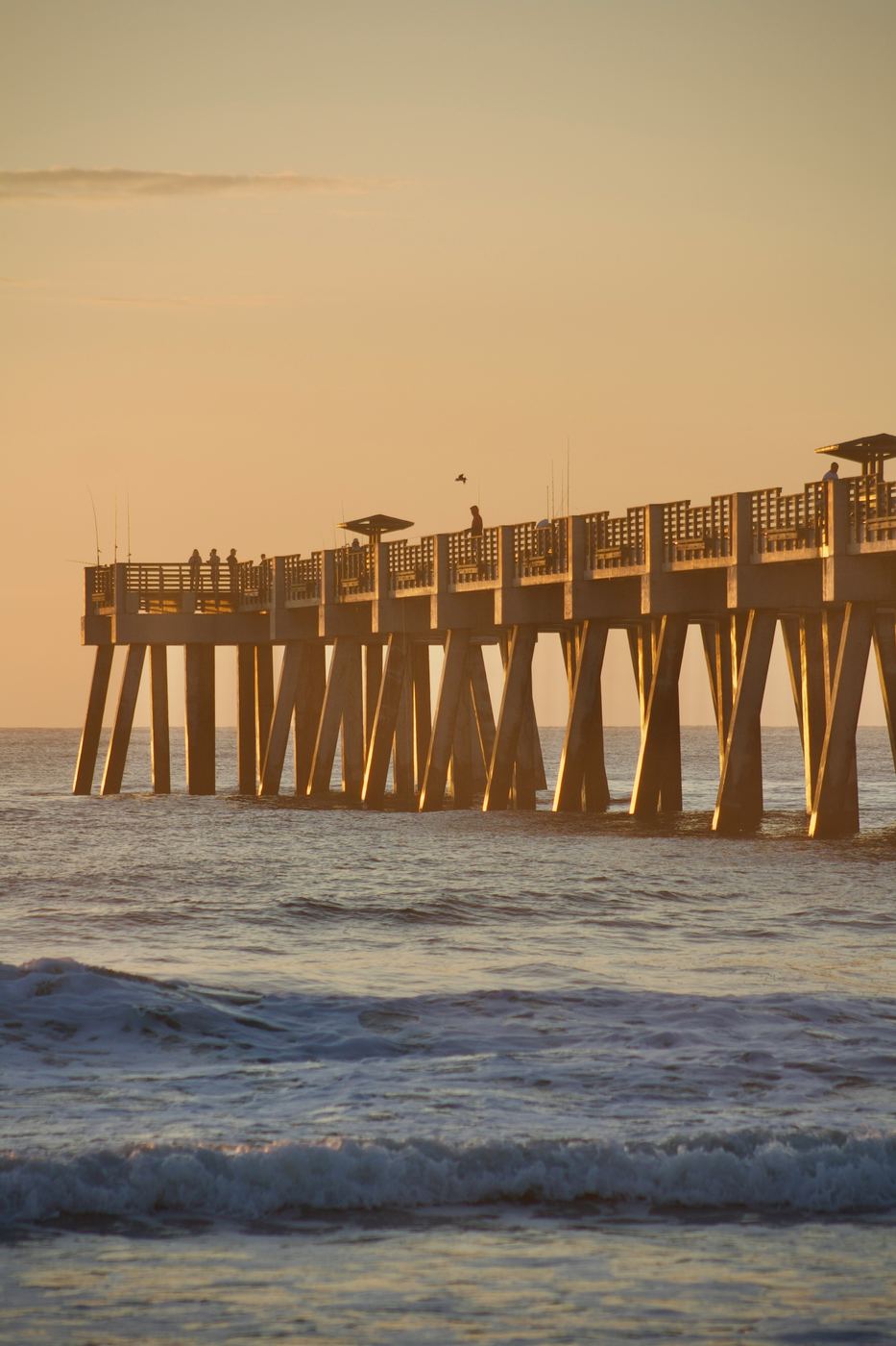 A fishing pier stretching over the Gulf at golden sunset